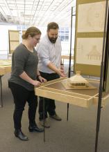 A woman and a man examine a small, wooden model of a building.