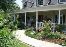 A sidewalk leads to a front porch through a shrub-filled landscape.