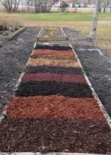 A rectangular garden bed with different colors of mulch divided into squares.