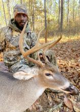 A man kneels beside a harvested buck.