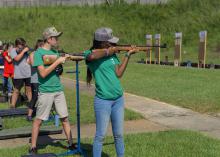 Teenagers at a shooting sports competition aim shotguns at targets.