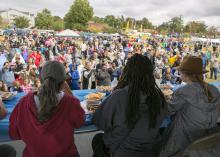 A large crowd gathers at a festival while a panel of judges tastes food.