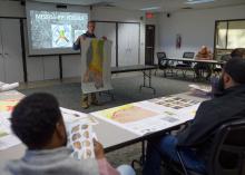 A person in the center of a meeting room shows a topographical map to others during a presentation.