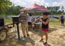 Jim McAdory, Mississippi State University Extension Service agent to the Mississippi Band of Choctaw Indians, shows Natasha Willis how to use the sunscreen dispenser provided by MSU Extension. The demonstration was part of a May 28 boating event in Neshoba County, Mississippi. (Photo by MSU Extension Service/Kevin Hudson)