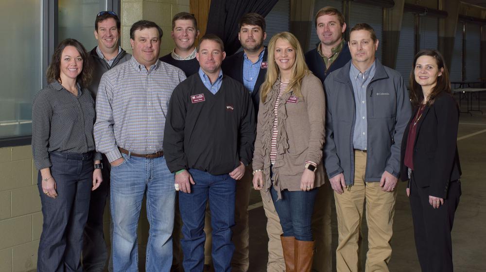 Ten adults, including 3 women and 7 men, stand smiling in front of a Mississippi Farmers’ Market banner.