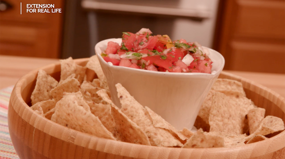 Homemade pico de gallo in a white container placed in the center of a wooden bowl of tortilla chips.