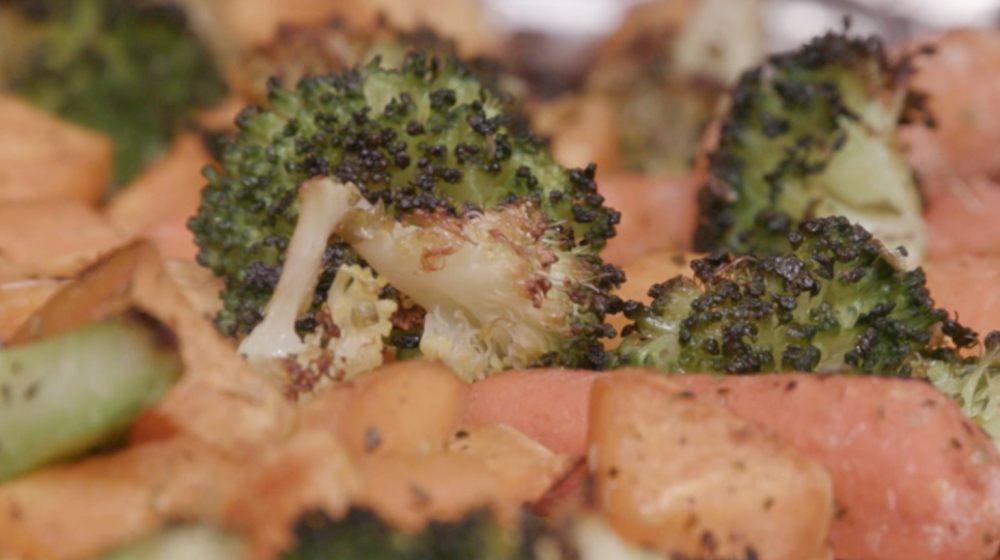 Roasted and seasoned broccoli florets, sweet potato chunks, and whole baby carrots on a foil covered sheet pan.