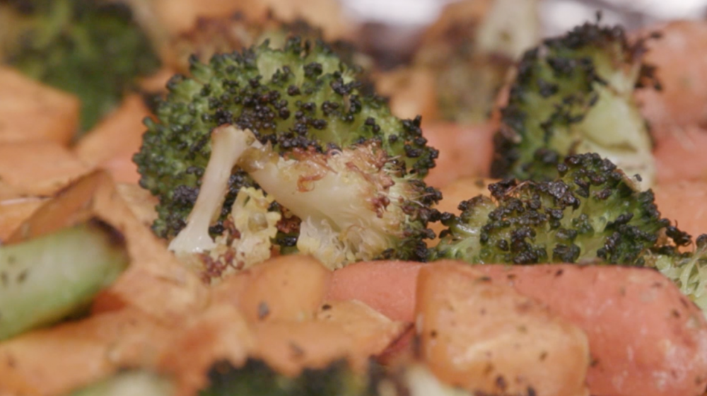 Roasted and seasoned broccoli florets, sweet potato chunks, and whole baby carrots on a foil covered sheet pan. 