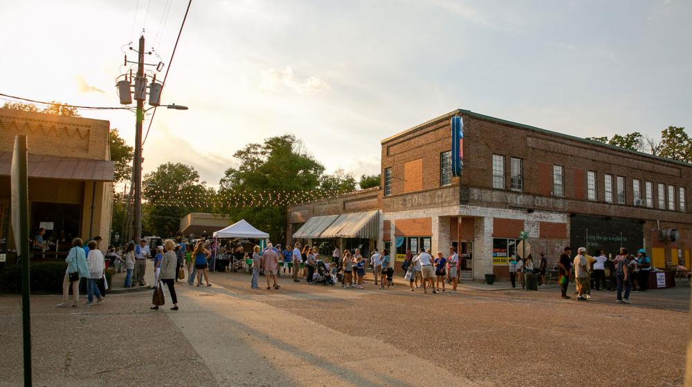 Sunset over a brick downtown filled with people milling about.