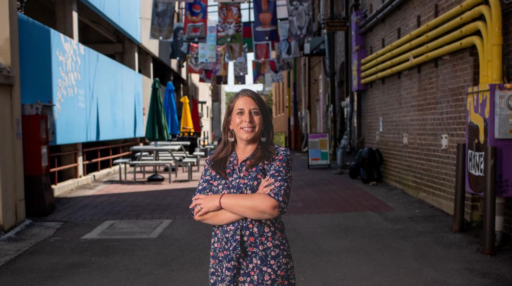 A woman smiling and standing on a street in front of many colorful, bright flags.