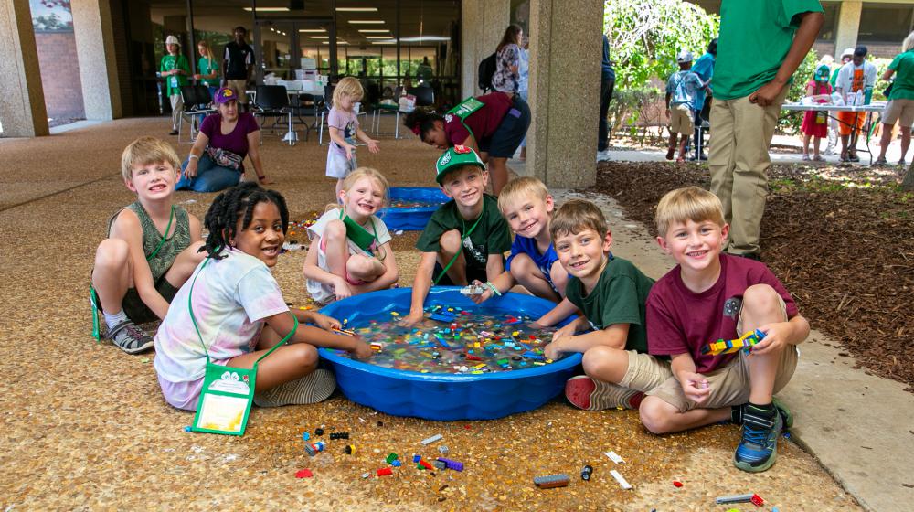Seven young children playing with legos in a small pool of water.
