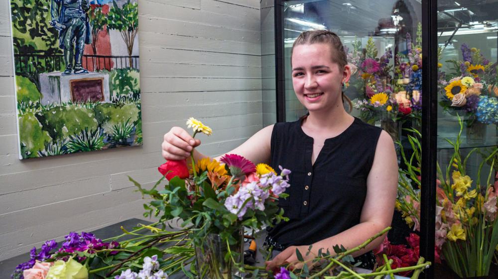 A young woman smiling while arranging a bouquet of flowers.