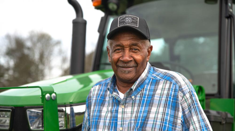 A smiling man standing in front of a green tractor.