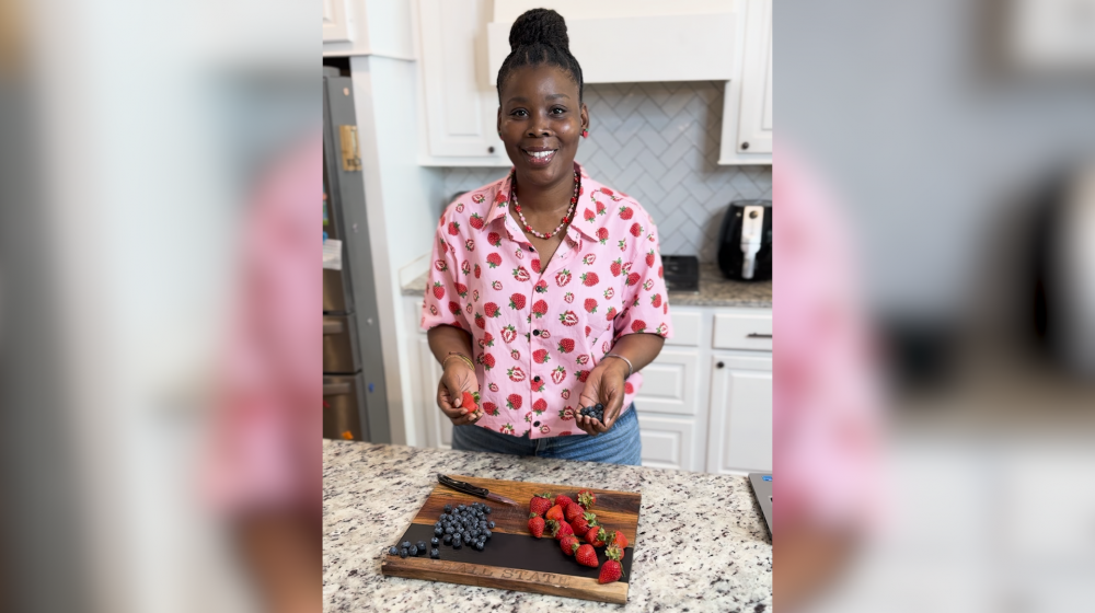 A woman stands in a kitchen with strawberries on a cutting board.
