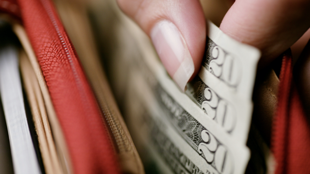 a closeup of a person taking $20 dollar bills out of a wallet