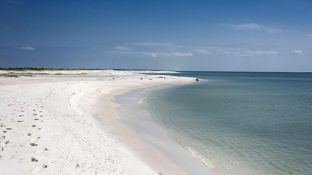 Dark blue water meets the edge of white sand on a clean, empty beach.