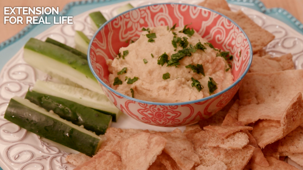 A plate with zuchinni, freshly baked chips, and a bowl of hummus in the center