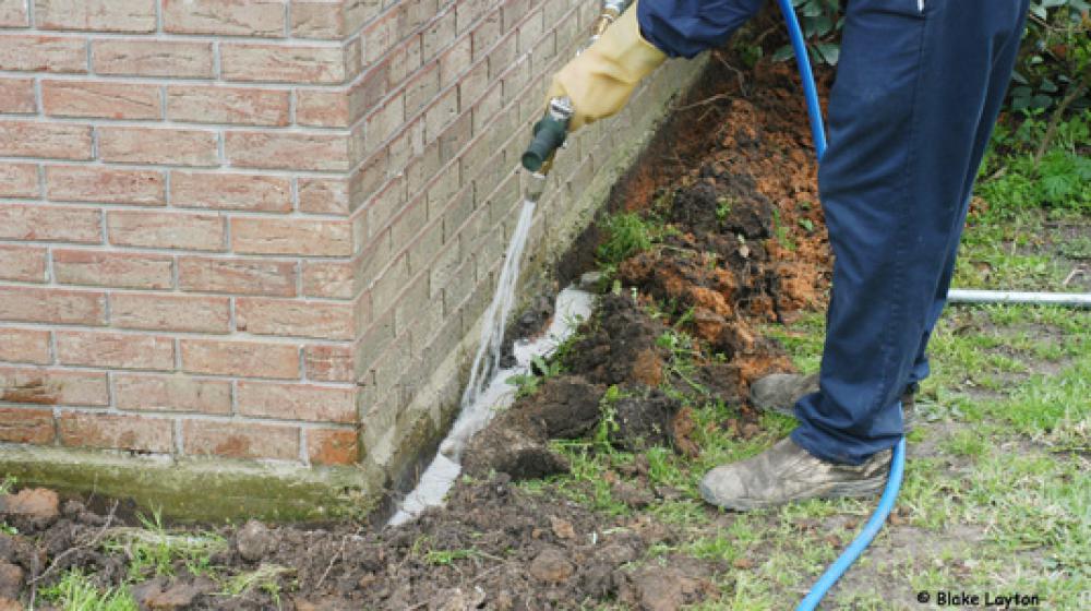 A pesticide technichian applies a termite treatment around a home foundation.