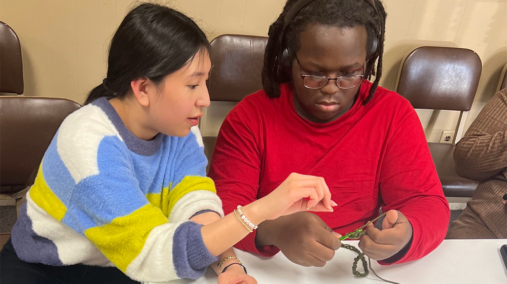 Woman showing another person how to crochet.