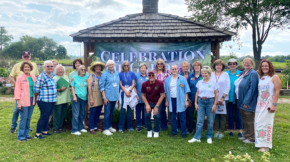 A group of 21 Master Gardeners standing in front of a rustic gazebo with a celebratory banner.