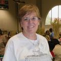 A woman stands smiling in front of a room full of people working at long tables.