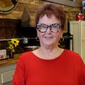 An elderly woman wearing animal print glasses and a bright red shirt stands smiling. Photo credit: Kevin Hudson