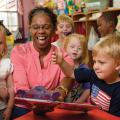 A woman happily reading a book to several small children.