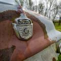 The front of an old Ford truck with the logo centered in an orange-colored rusty area of the light blue truck. 