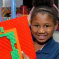 A young girl smiles and holds up a Lego creation.
