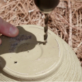 Fingers steady an upside-down flower pot as a drill bit pierces the bottom to make drainage holes. 