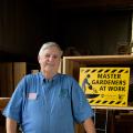 Paul Cavanaugh standing in front of a sign that reads Master Gardeners at Work.