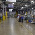 A line of four people walking in a room full of machinery and boxes.