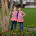 Two young girls with red hair and matching pink shirts stand next to each other with a hand on the hip.