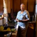 A woman wearing a white and blue striped shirt and holding fresh vegetables stands in front of a kitchen sink.