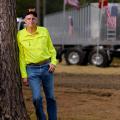 A man wearing a bright yellow button-up shirt leans against a large truck and rests one hand in his blue jean pocket.