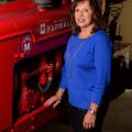 A smiling woman wearing a blue shirt stands next to and rests her arm on a red piece of machinery. 