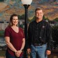 A woman and a man standing in front of a mural and lamppost.