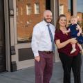 A man, woman, and child standing outside, smiling in front of a building.