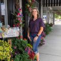 A woman standing outside beside flowers wreathing a door.