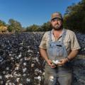 A man wearing overalls and standing in a blooming cotton field.