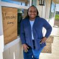 A woman standing beside the window of a house that has a sign with “Venisha’s Home” listed on it.