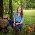 A girl wearing denim smiles as she feeds her chickens.