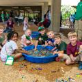 Seven young children playing with legos in a small pool of water.