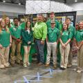 A large group of people, standing, smiling, and wearing green shirts.