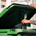 A person throwing a trash bag into a trash can.