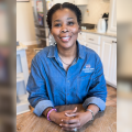 A woman sits at a kitchen table and smiles for the camera.