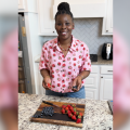 A woman stands in a kitchen with strawberries on a cutting board.
