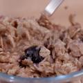 A small clear glass bowl holds baked oatmeal with blueberries and a stainless steel spoon.