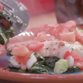 Baked fish with spinach, tomatoes, and onions sits on a plate.