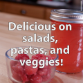 A clear glass bowl of red raspberries sits on a butcher block table in front of a pint clear glass jar filled with homemade raspberry vinegar and topped with a metal lid and ring. Text overlay reads, "Delicious on salads, pastas, and veggies!"